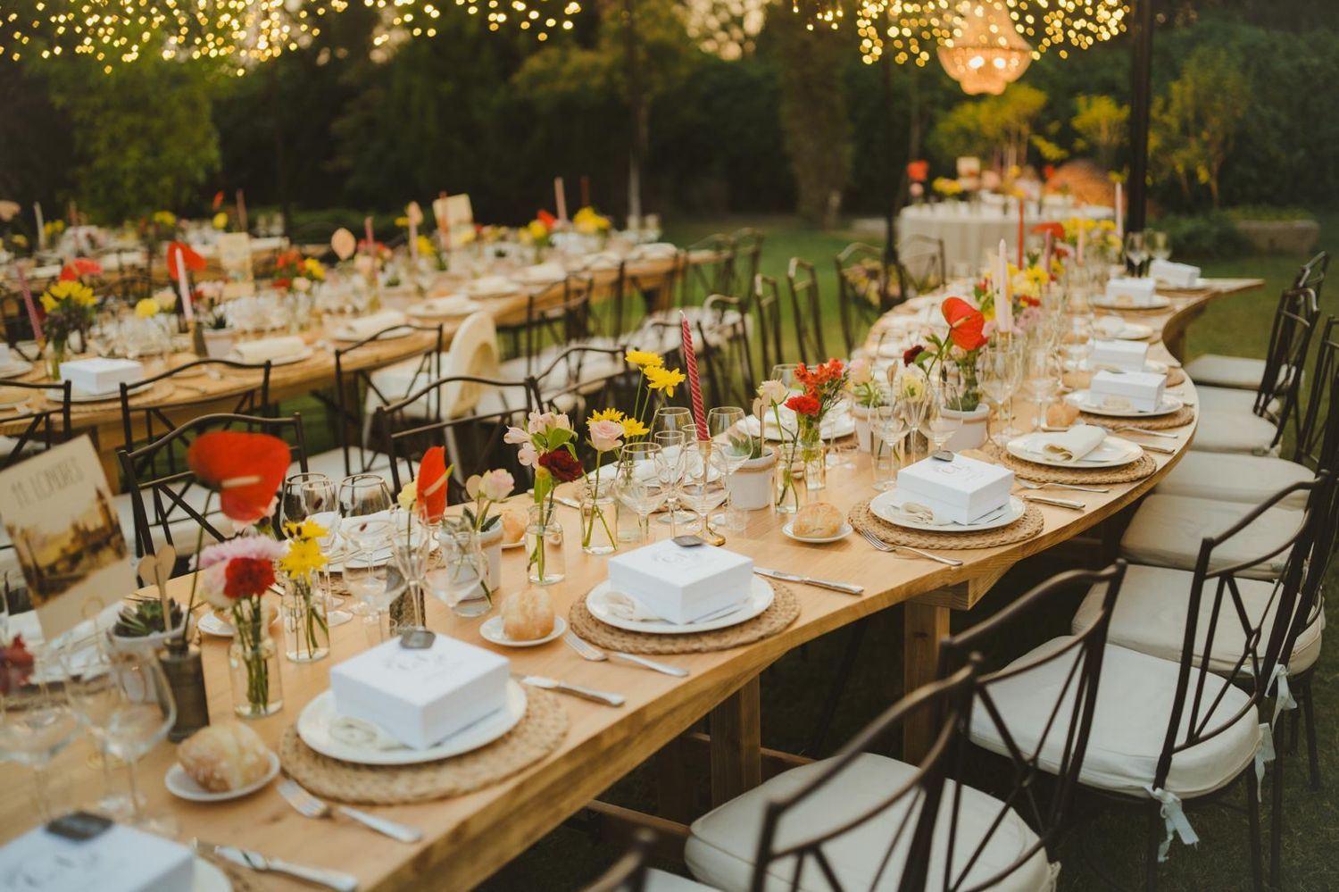 Mesa de madera curvada con flores pequeñas y vajilla blanca