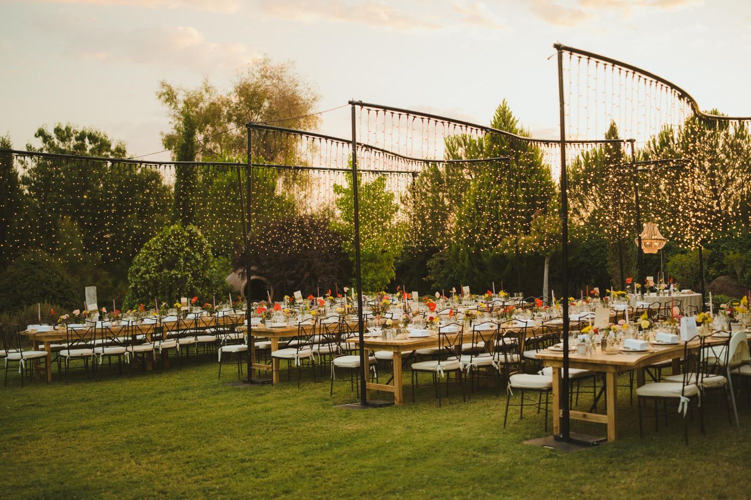 Jardín con cortinas de luz y mesas largas al atardecer